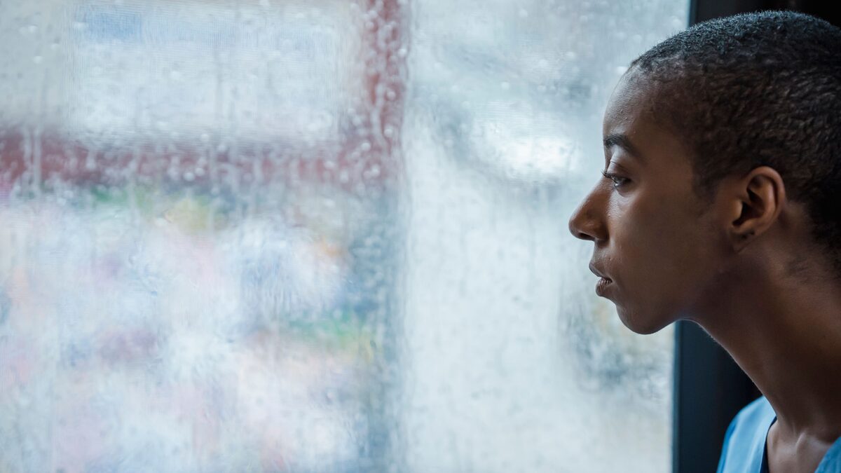 A person sitting by a window at dusk with headphones on, looking calm and reflective