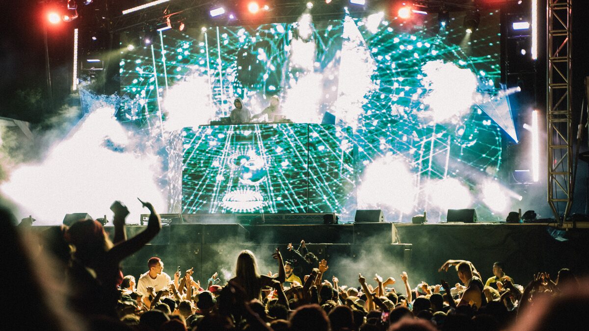 Festival crowd with hands raised under bright stage lights during a night set