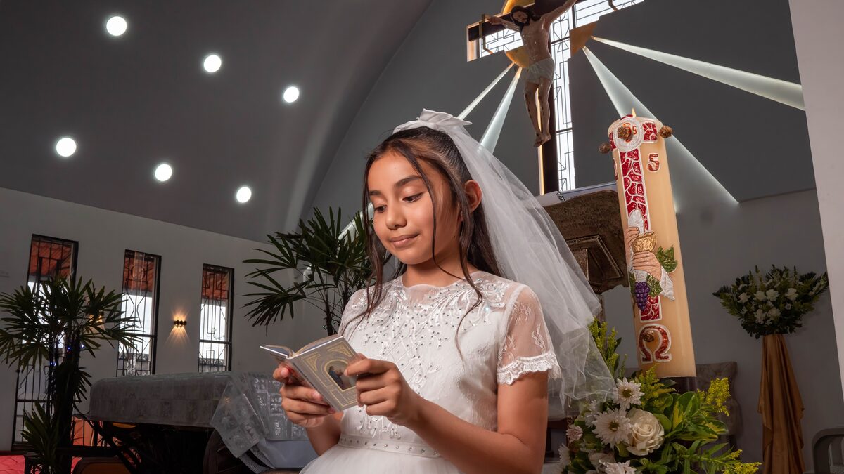 A child dressed in white reading quietly in a gentle, reverent first communion moment