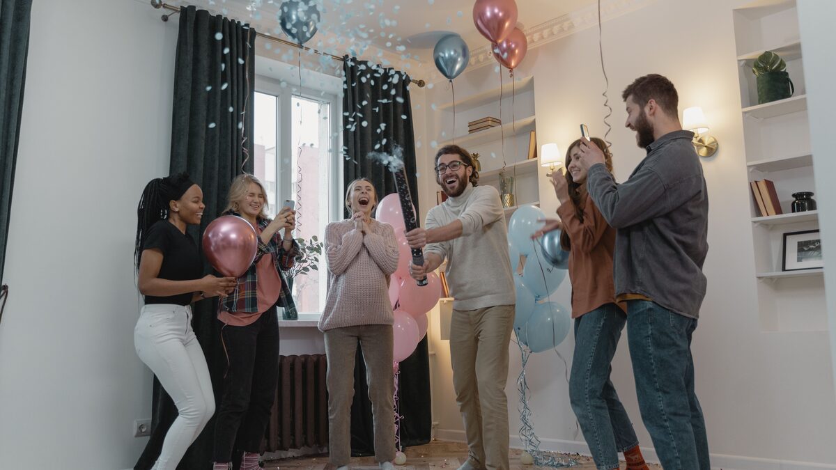 Friends and family celebrating at a gender reveal party with pink and blue balloons and confetti