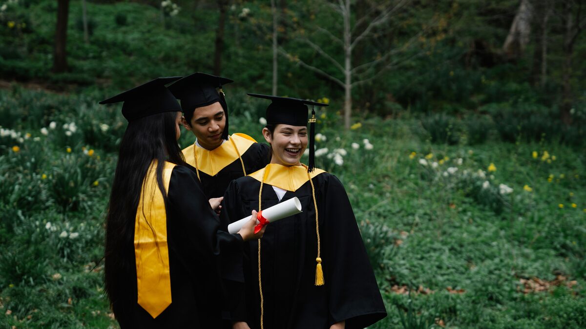 A graduate in cap and gown holding a phone, smiling at a celebration