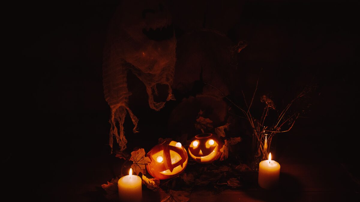 Carved jack-o-lanterns glowing on a porch with fog and string lights at night