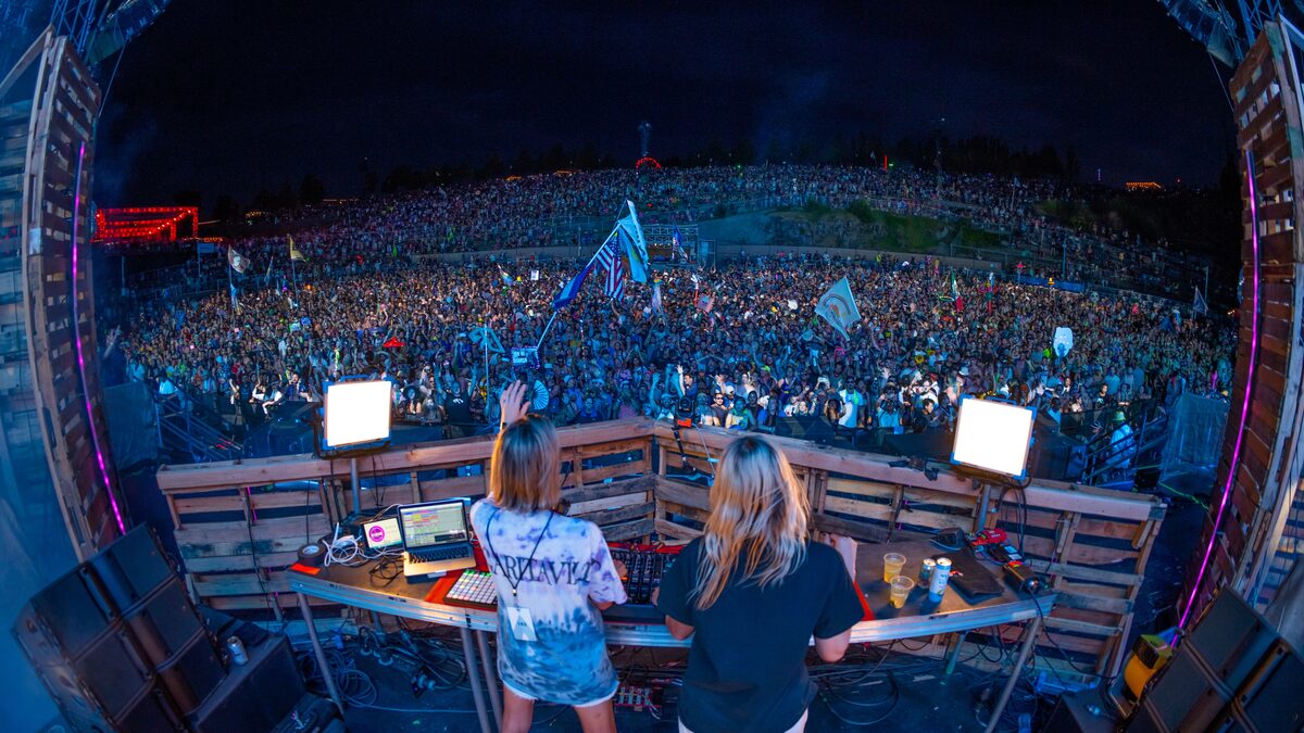A crowd with hands raised under bright strobe lights at a festival