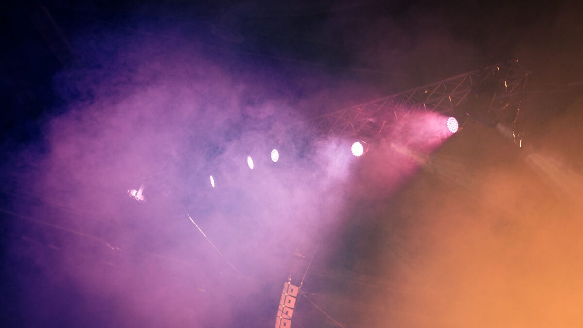 Bright neon stage lights over a concert crowd with hands raised