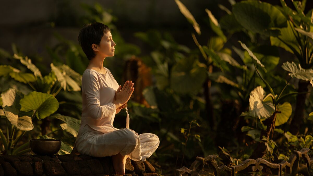 A person sitting cross-legged on a mat in a quiet room with soft light
