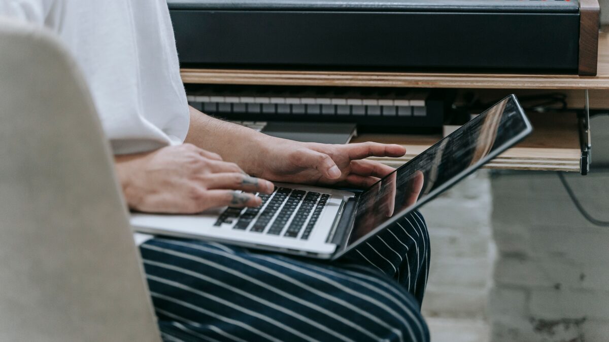 A musician working at a laptop with headphones, preparing tracks for upload