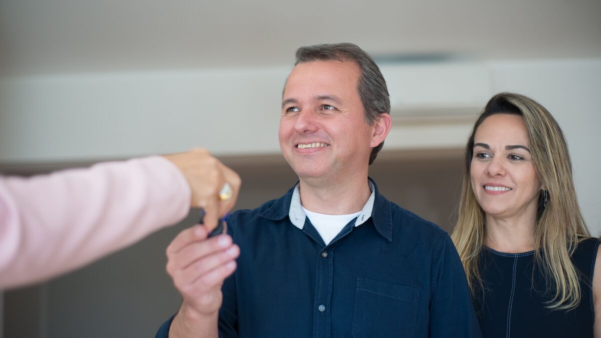 A couple holding keys and boxes in the doorway of their new home
