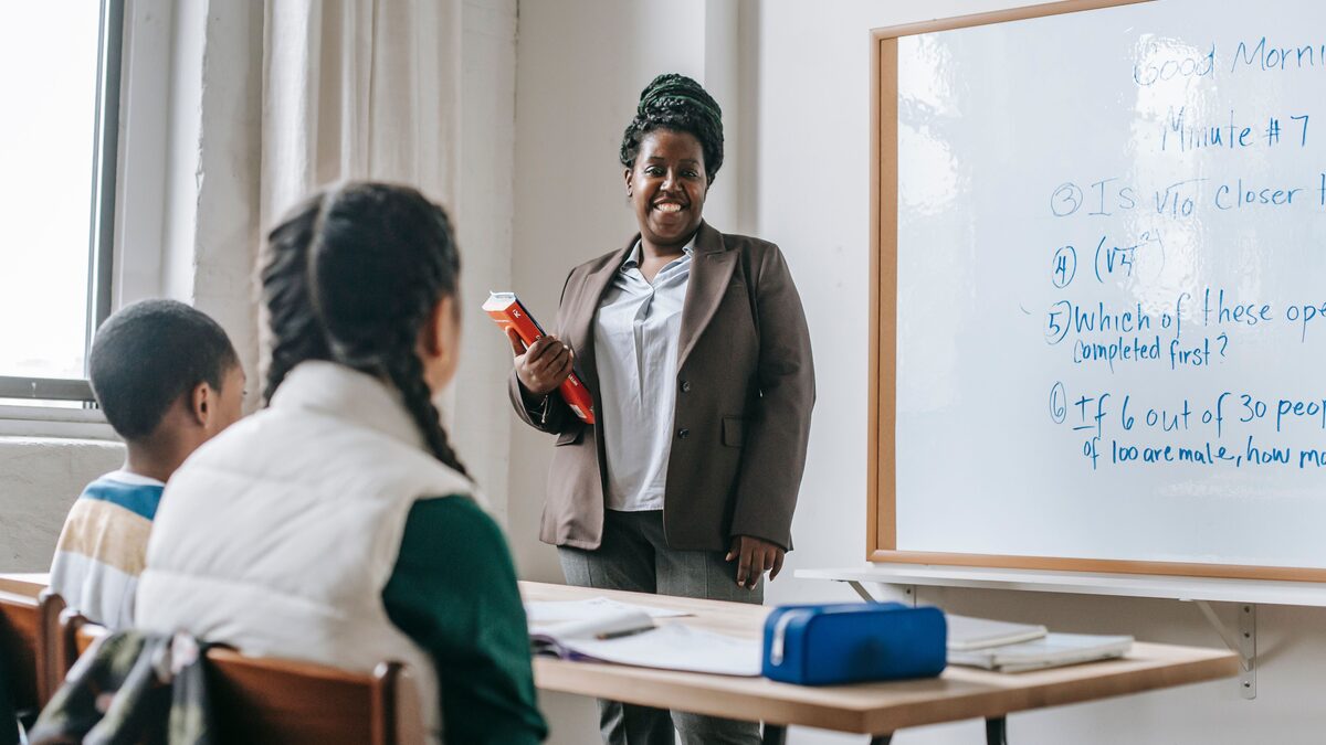 A teacher smiling with students in a bright classroom