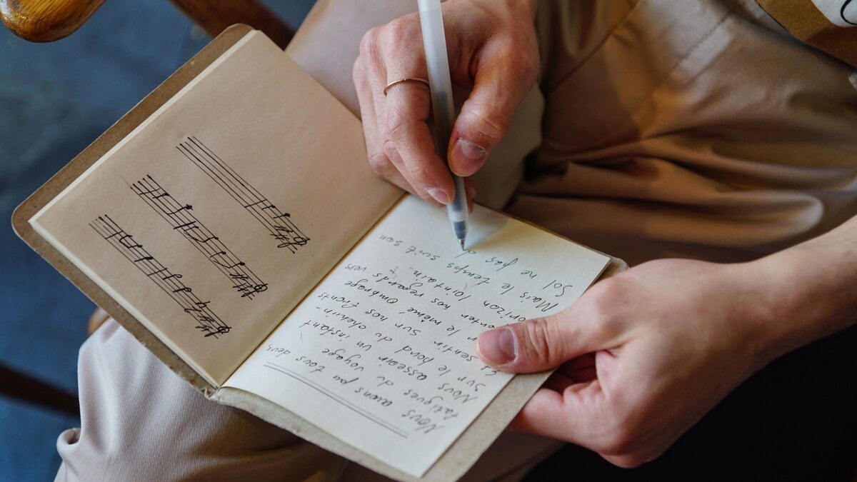 Notebook of handwritten lyrics beside a laptop and headphones
