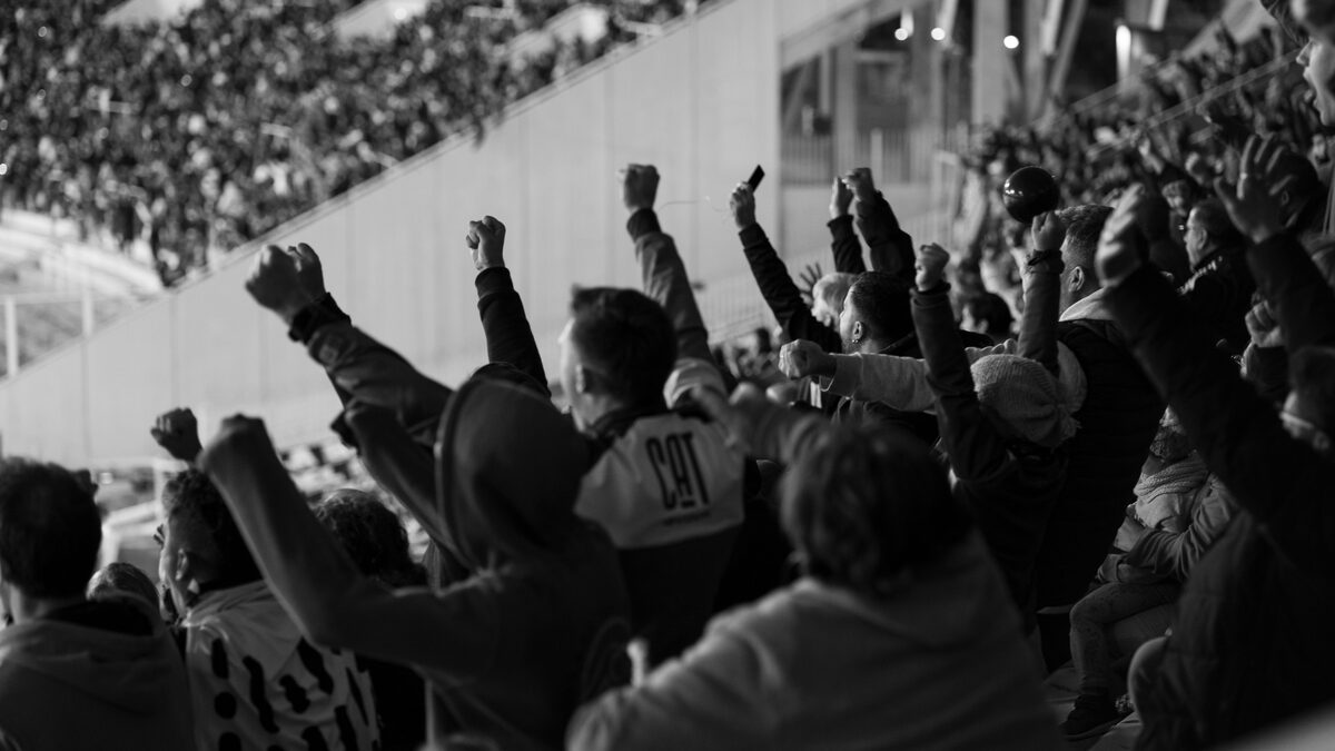A packed stadium crowd standing and cheering under bright floodlights at night