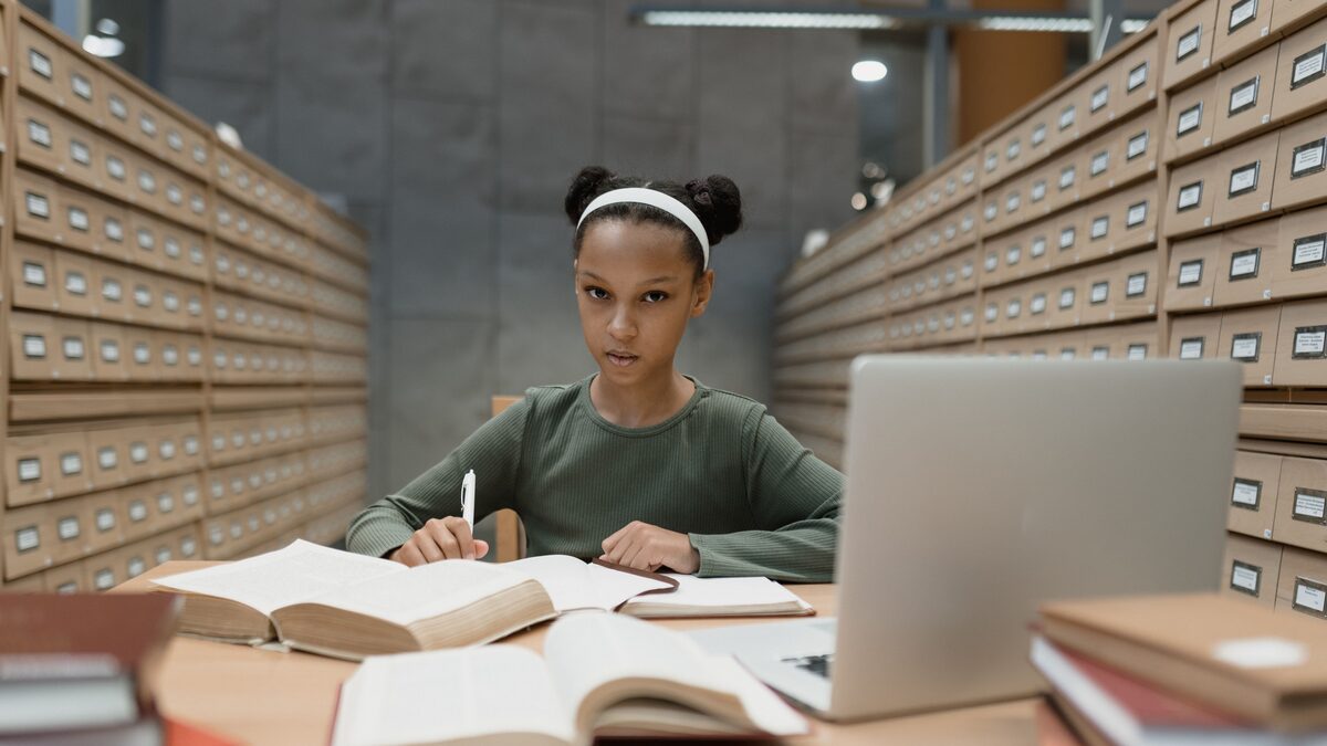A student at a desk with headphones on, books and a laptop under warm light