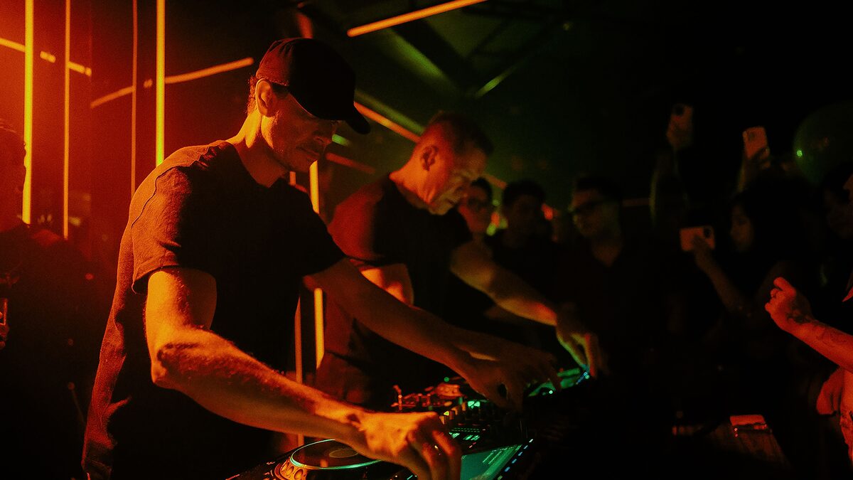 Dark techno club at peak time with strobe lights over a packed dancefloor