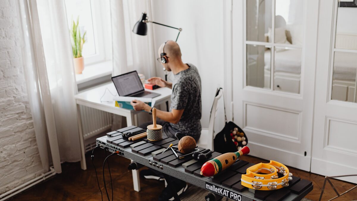 A musician working at a home studio desk with a laptop, keyboard and headphones