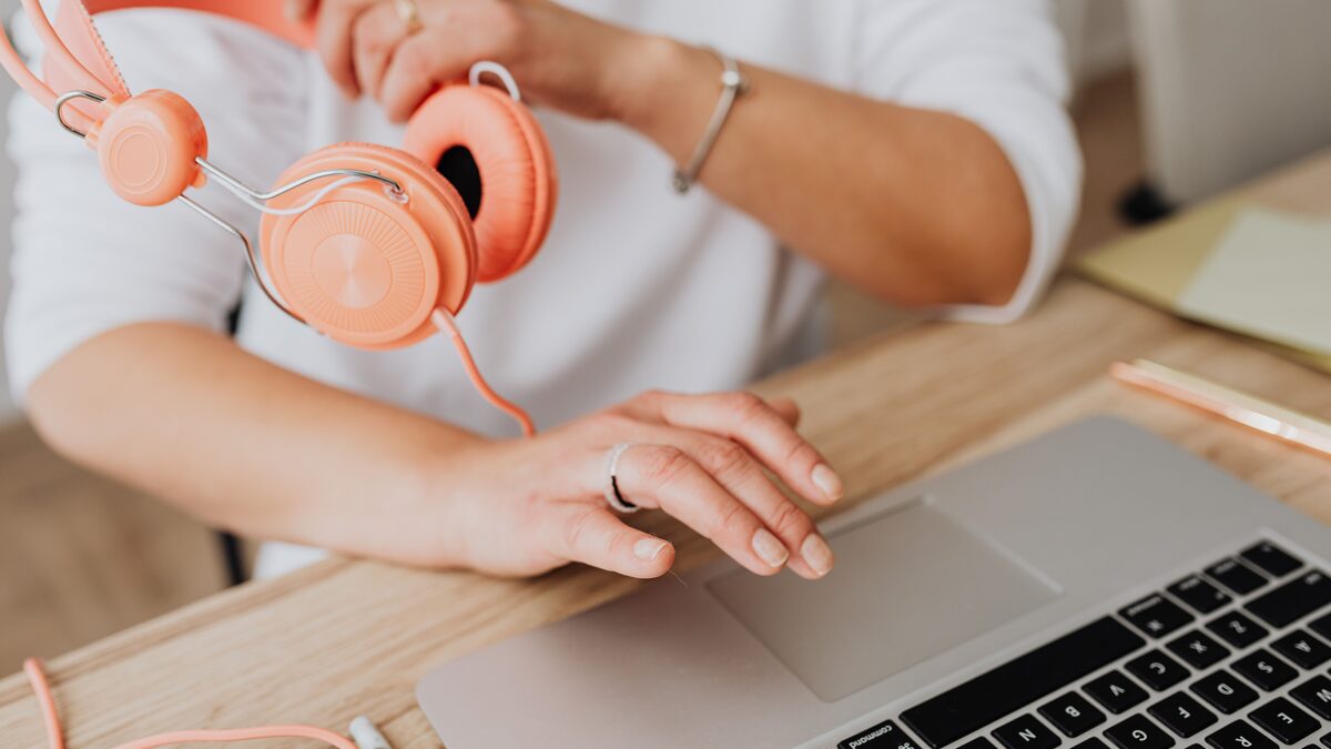 A pair of over-ear headphones resting on a desk beside a laptop showing an audio waveform