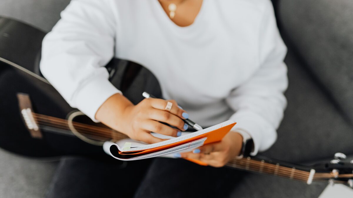 Songwriter sketching a song arrangement in a notebook beside a guitar