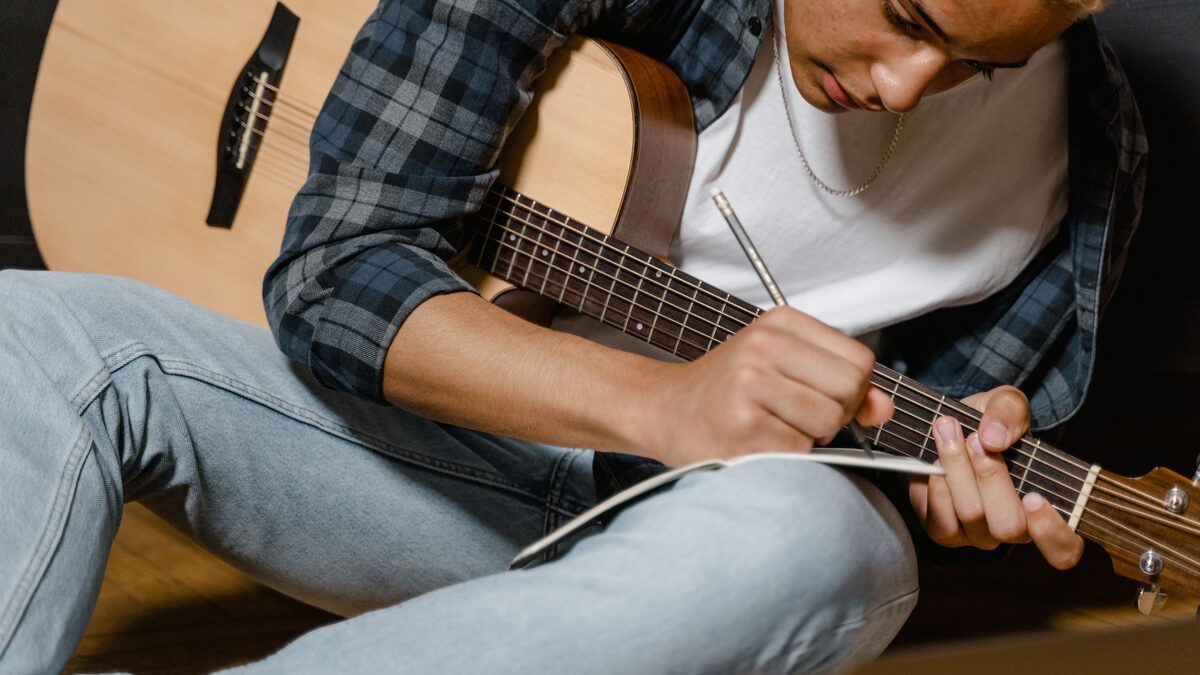 Songwriter writing lyrics in a notebook with a guitar nearby